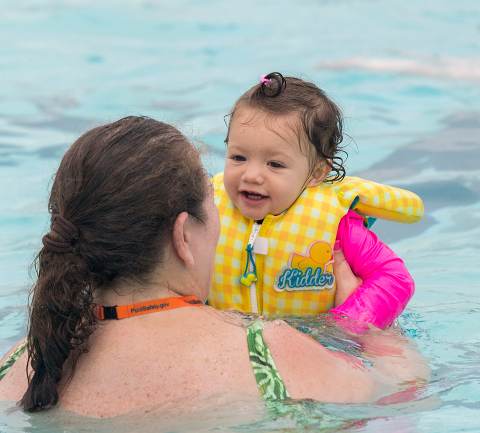 Young girl swimming with mom in pool.