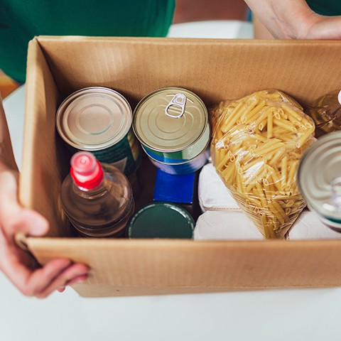 A cardboard box of cans and pasta being handed over to someone in need.