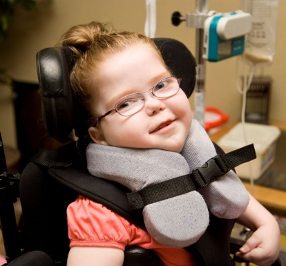 A girl with special needs strapped in to a wheelchair with a special cushion to hold her head up. 