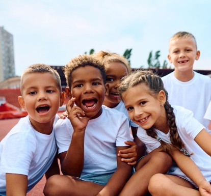 a diverse group of smiling children in white t-shirts.