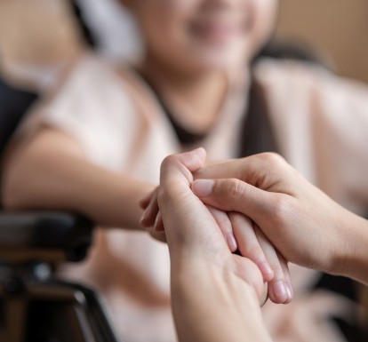 Close-up of a parent holding the hand of a child who's in a wheelchair.