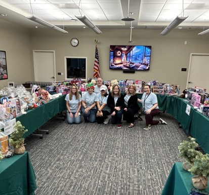 Members of the CSC Volunteering Committee kneel in front of tables full of toys for the first-ever Holiday Pop-Up Event in 2025.
