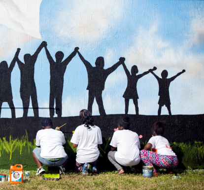 Youth from a local Teen Outreach Program paint a mural of children holding hands.