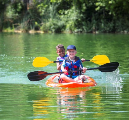 Two boys wearing life jackets in a kayak smiling while rowing through a river.