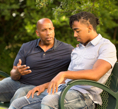 A mentor and teen sit on a bench together talking.