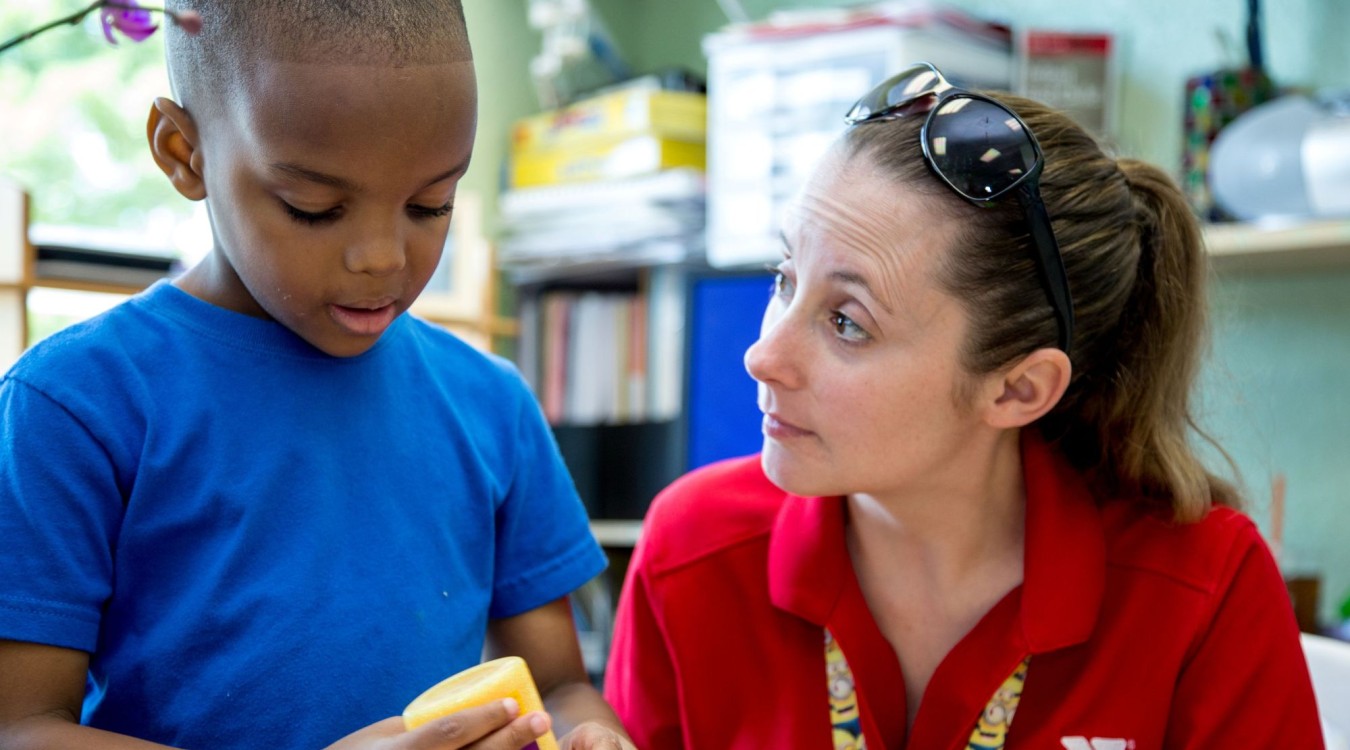 Little boy concentrates on an art project with the help of a kind child care teacher.