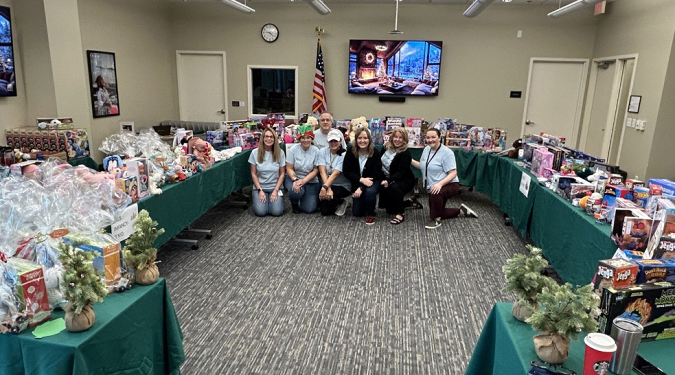 Members of the CSC Volunteering Committee kneel in front of tables full of toys for the first-ever Holiday Pop-Up Event in 2025.