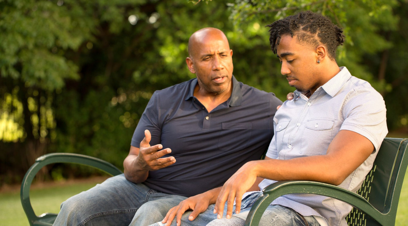 A mentor and teen sit on a bench together talking.