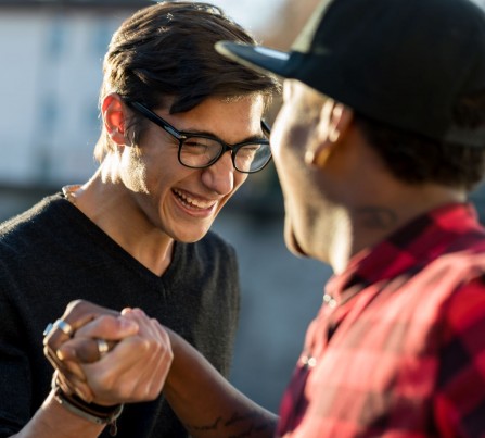 A young man and a mentor grab hands and smile at each other outside.