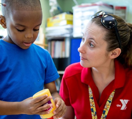 Little boy concentrates on an art project with the help of a kind child care teacher.