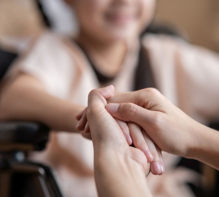 Close-up of a parent holding the hand of a child who's in a wheelchair.
