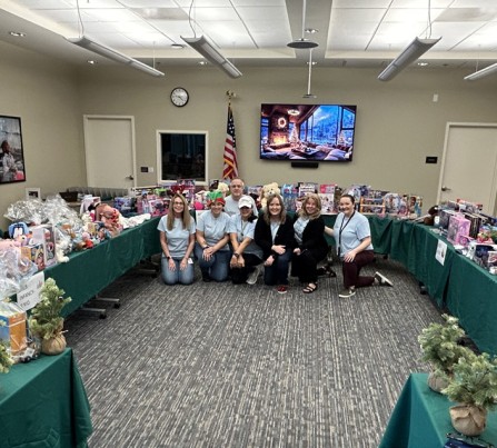 Members of the CSC Volunteering Committee kneel in front of tables full of toys for the first-ever Holiday Pop-Up Event in 2025.