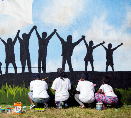 Youth from a local Teen Outreach Program paint a mural of children holding hands.
