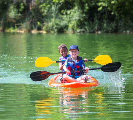 Two boys wearing life jackets in a kayak smiling while rowing through a river.