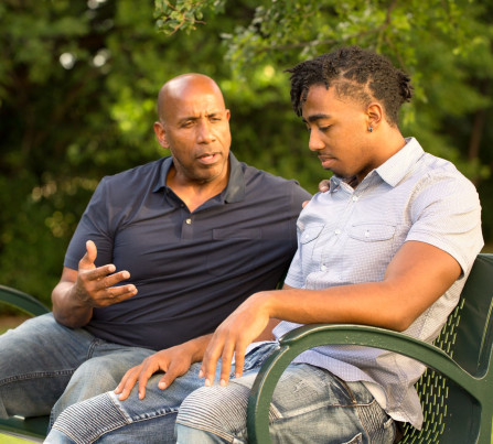 A mentor and teen sit on a bench together talking.