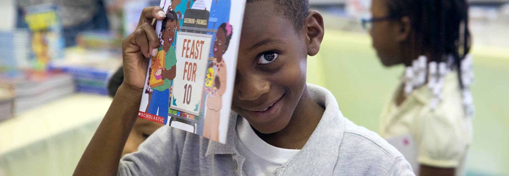 Little boy smiling holding up a book.