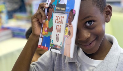 Little boy smiling holding up a book.