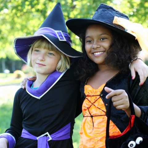 Two smiling school-age girls, dressed as witches, with their arms over each other's shoulders as they trick-or-treat.