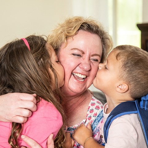 Grandchildren kissing grandmother on cheeks.