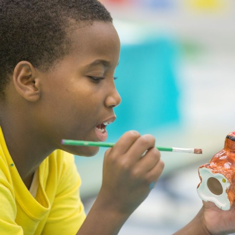 A little boy in a yellow T-shirt paints a ceramic dog at summer camp.