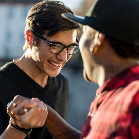 A young man and a mentor grab hands and smile at each other outside.