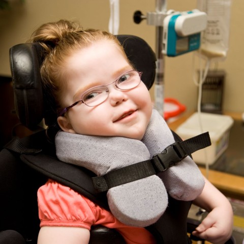 A girl with special needs strapped in to a wheelchair with a special cushion to hold her head up. 