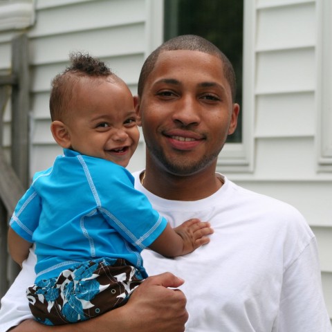 A smiling father holds his happy toddler son in his arms.