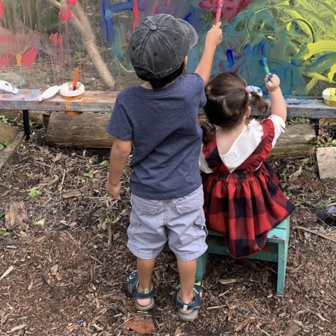 A little boy and girl in a garden painting a wall. 