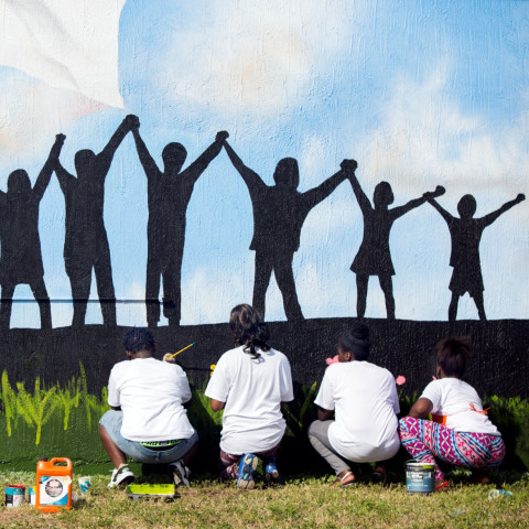 Youth from a local Teen Outreach Program paint a mural of children holding hands.