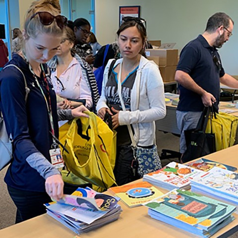 A room full of Palm Beach County public school teachers choose books laid out on a table for Booksgiving.