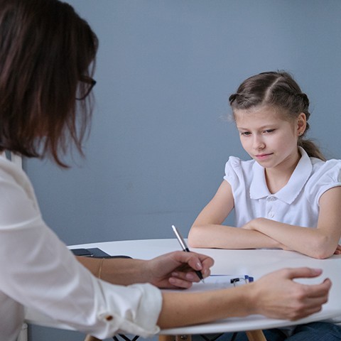 Serious little girl sitting at a table with a mental health counselor.