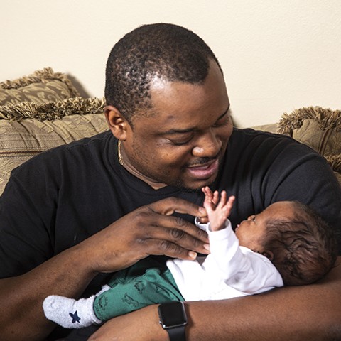 Dad cradles newborn baby in his arms, making eye contact.
