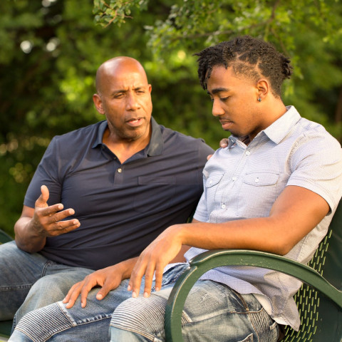 A mentor and teen sit on a bench together talking.